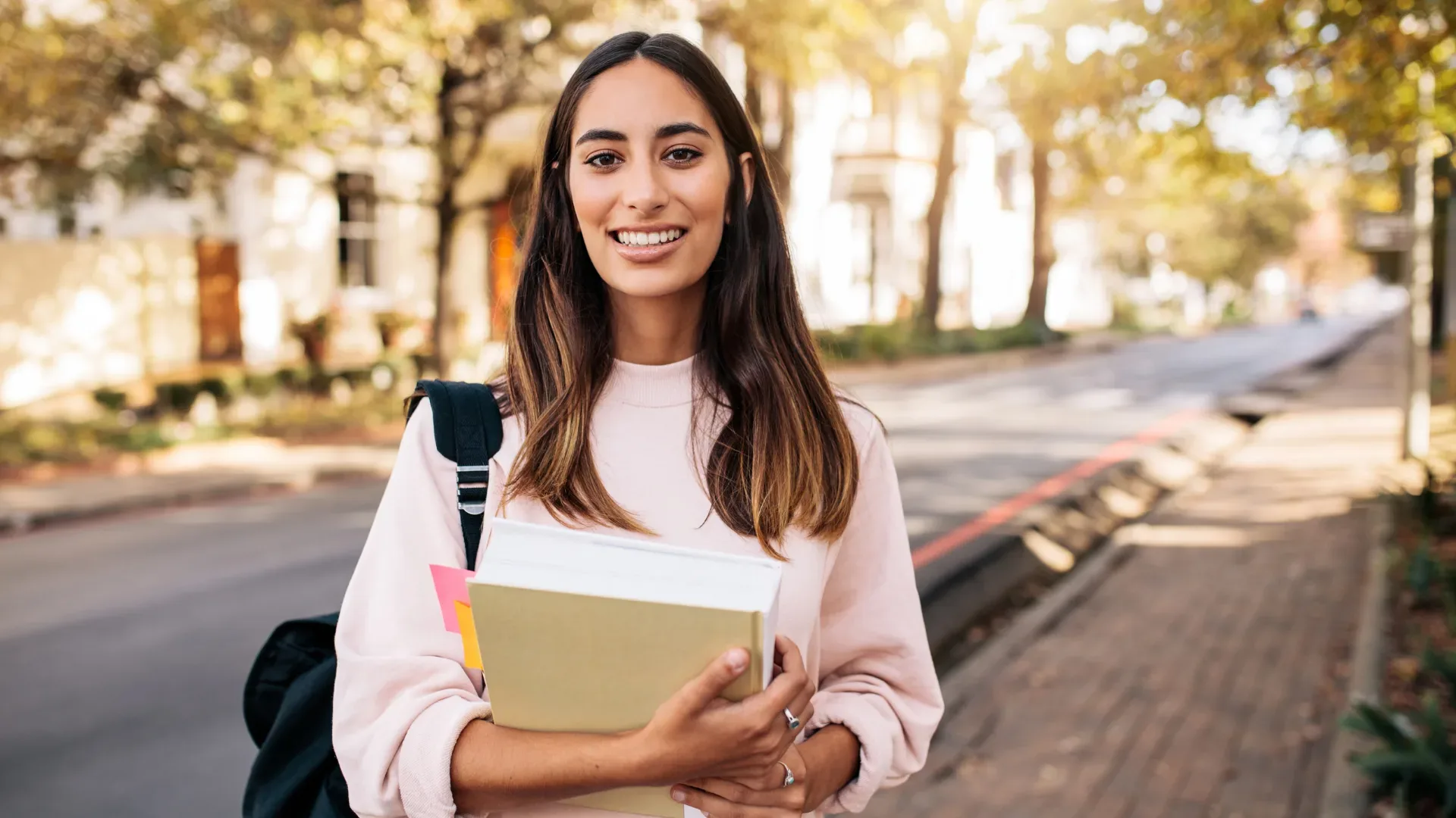 Student holding her notebook and looking at camera with university in background