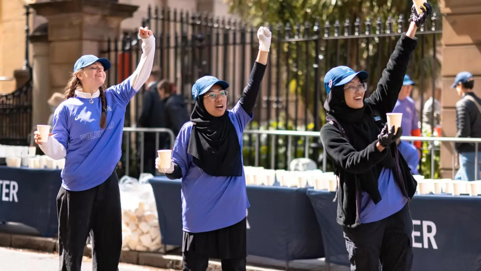 TCS Sydney Marathon volunteer marshalls on side of the road holding cups of water and cheering on runners