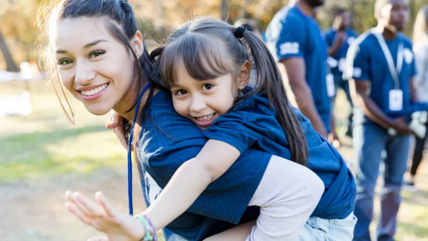 Volunteer piggy backing a child volunteer at an outdoor event - both smiling at camera