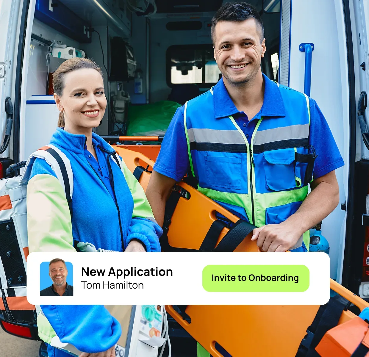 Two volunteers - one holding a stretcher - out front of ambulance, smiling at camera