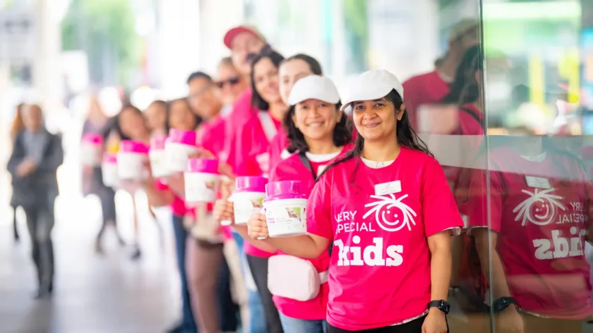 Very Special Kids volunteers dressed in pink tshirts holding donation tins for a fundraiser smiling at camera