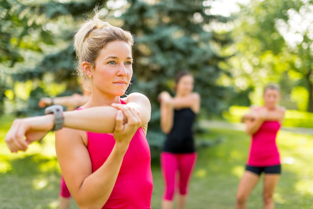 Portrait of a concentrated young woman streching her arm before jogging with friends