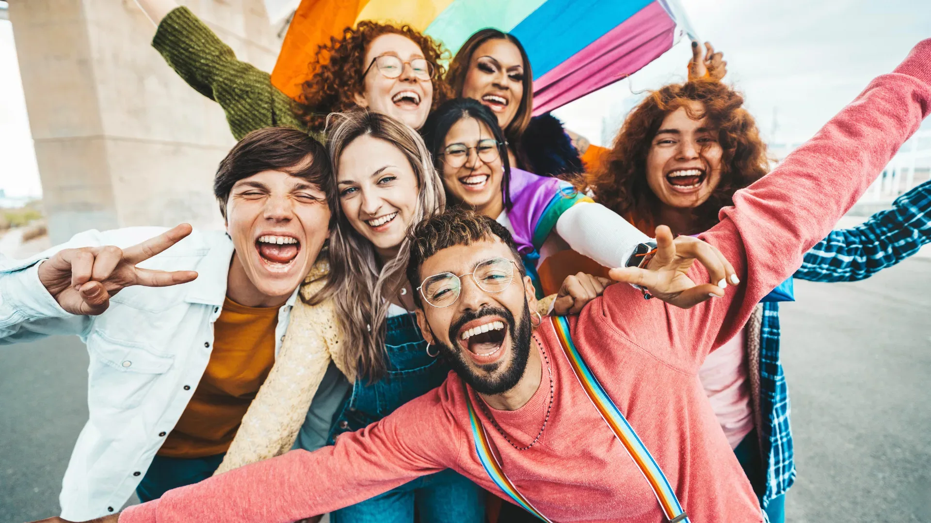 Group of diverse young people smiling in front of rainbow flag