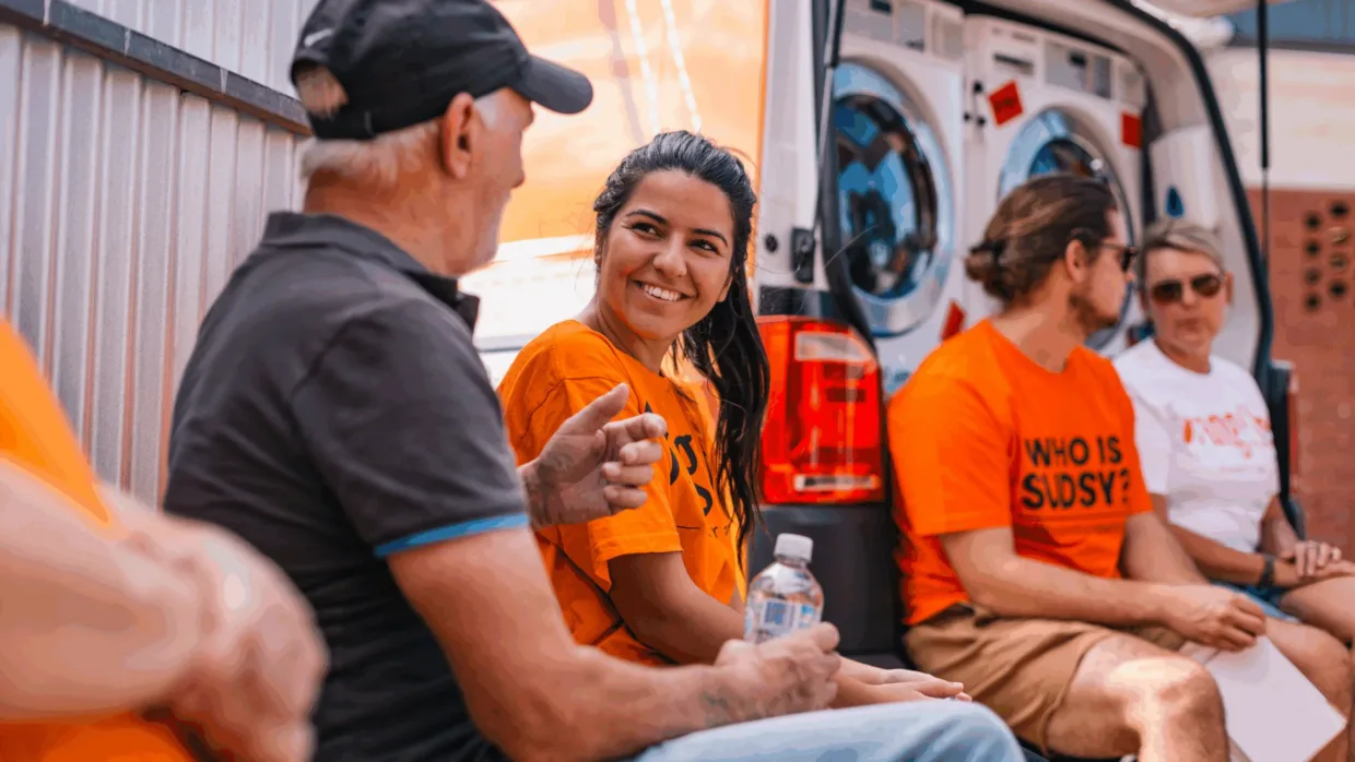 Orange Sky volunteer smiling and talking to one of the Orange Sky 'friends' out the front of a mobile laundry