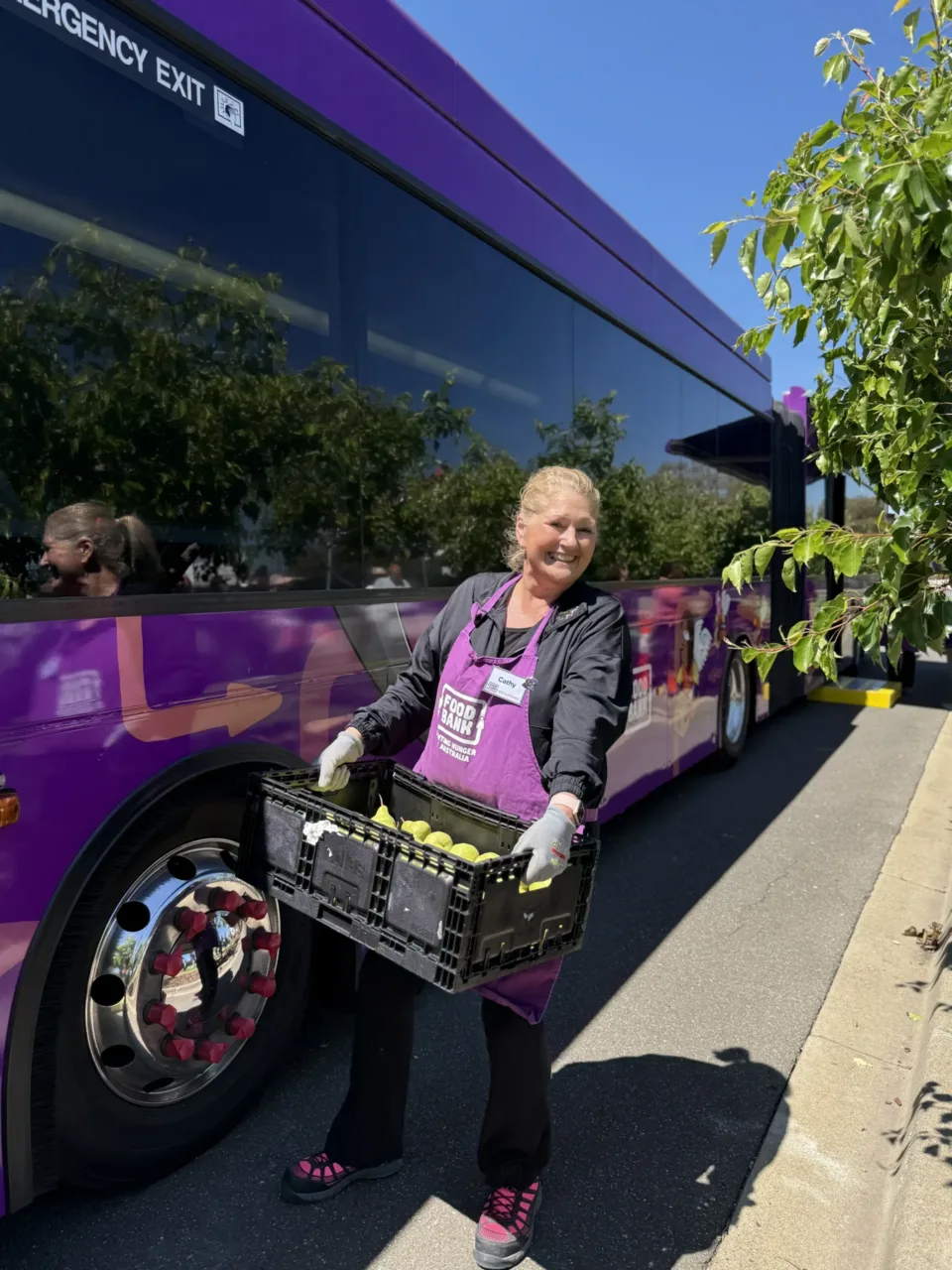 Foodbank Victoria volunteer holding a crate of food in front of a bus