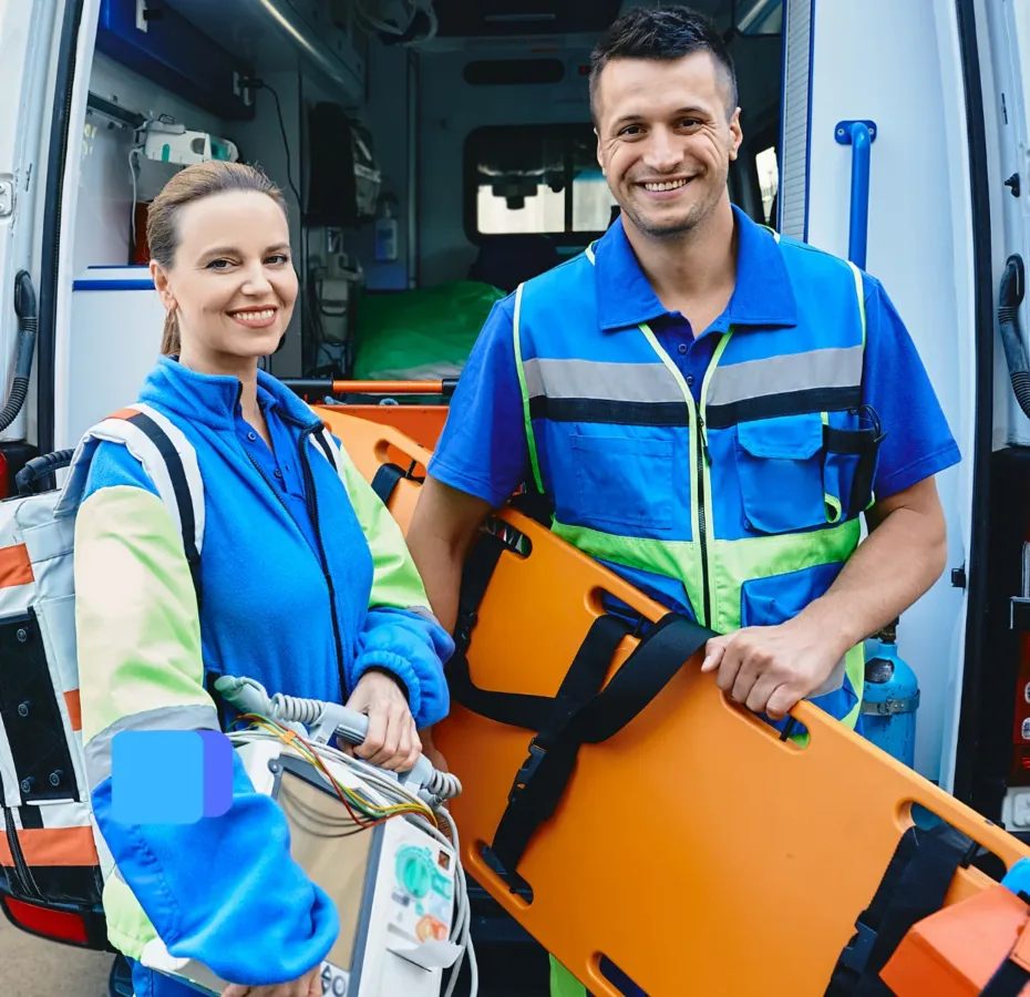 Two volunteers - one holding a stretcher - out front of ambulance, smiling at camera