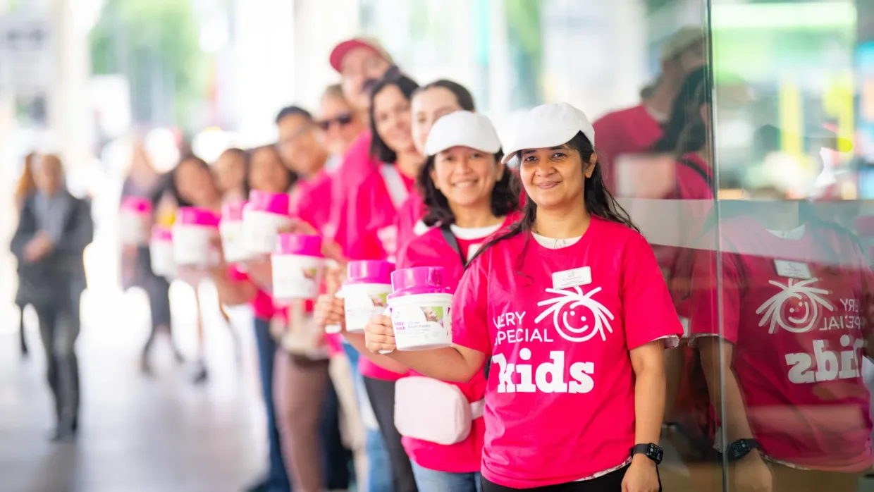 Very Special Kids volunteers in bright pink tshirts holding collection tins for a fundraising event