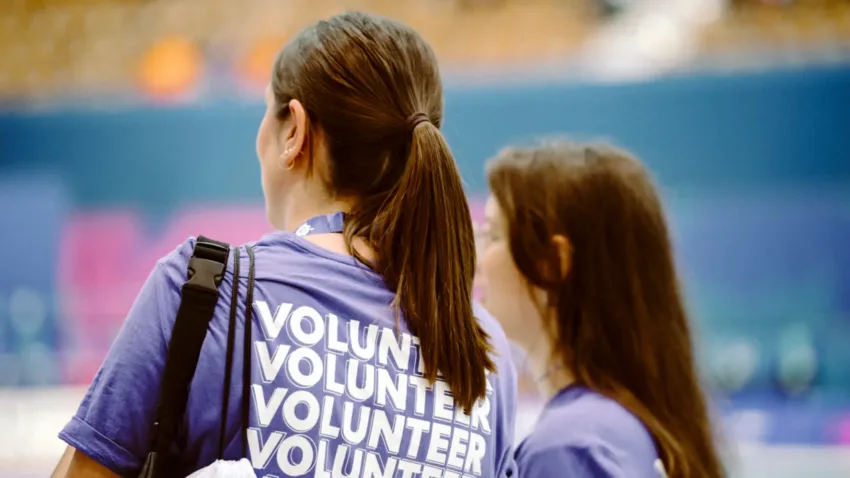 Two volunteers wearing purple tshirts with volunteer written on the back. Volunteers are only shown from their back