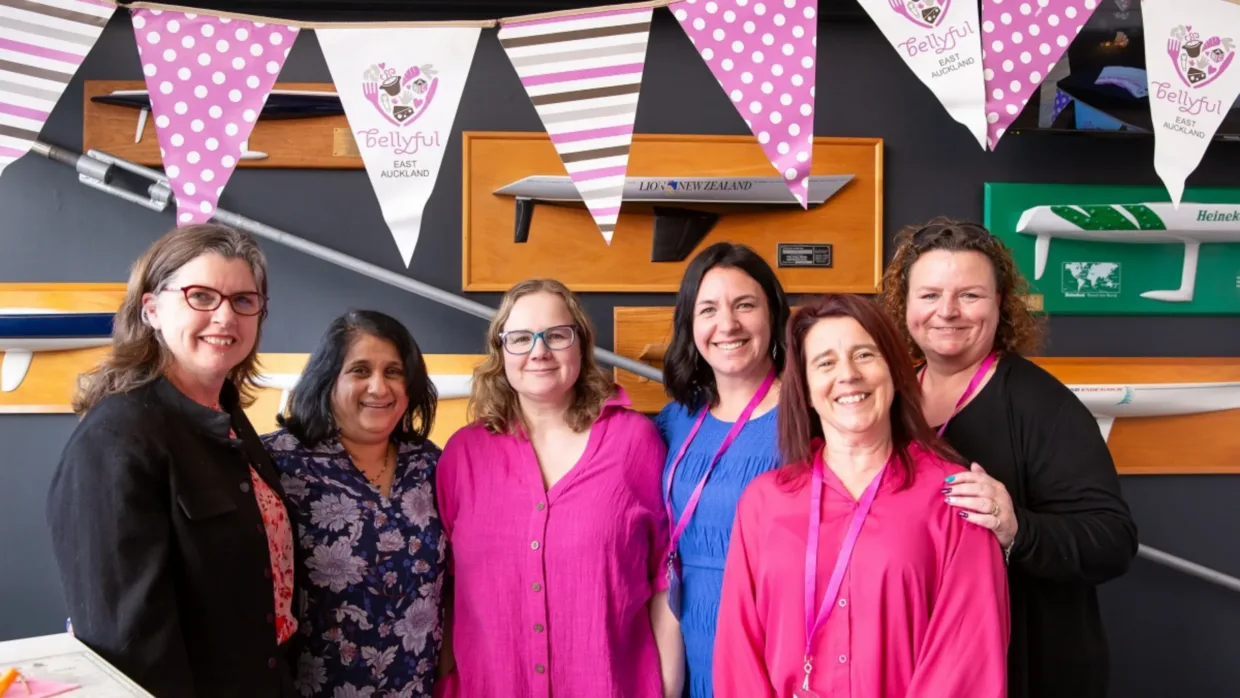 Group of Bellyful NZ volunteers smiling at camera with festive flags flying overhead