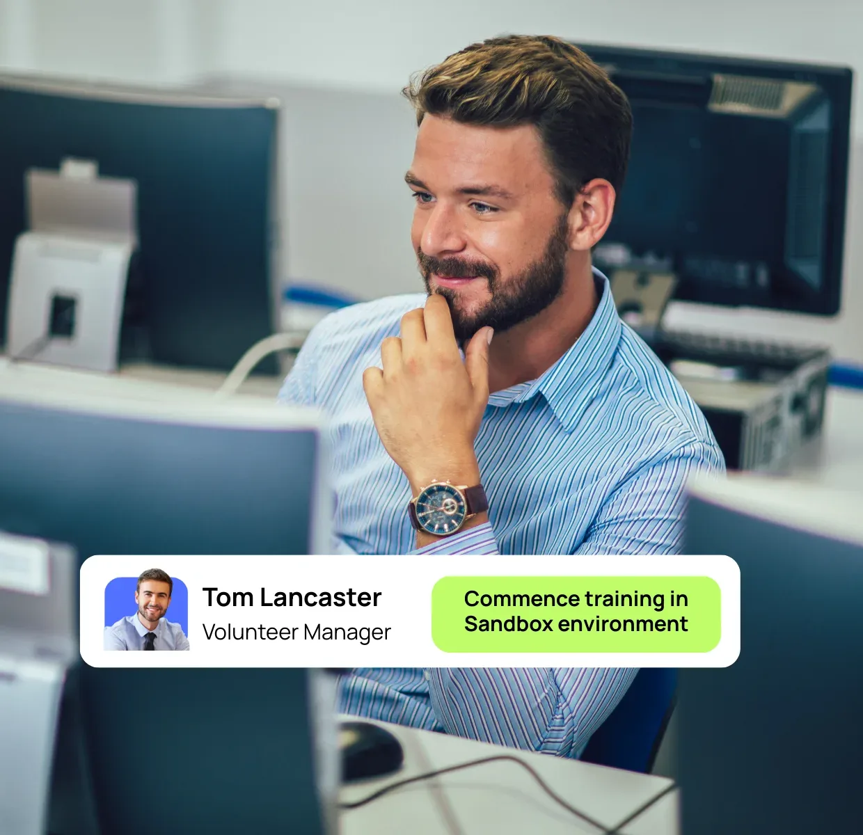 Man working in the office surrounded by computers smiling at his computer screen