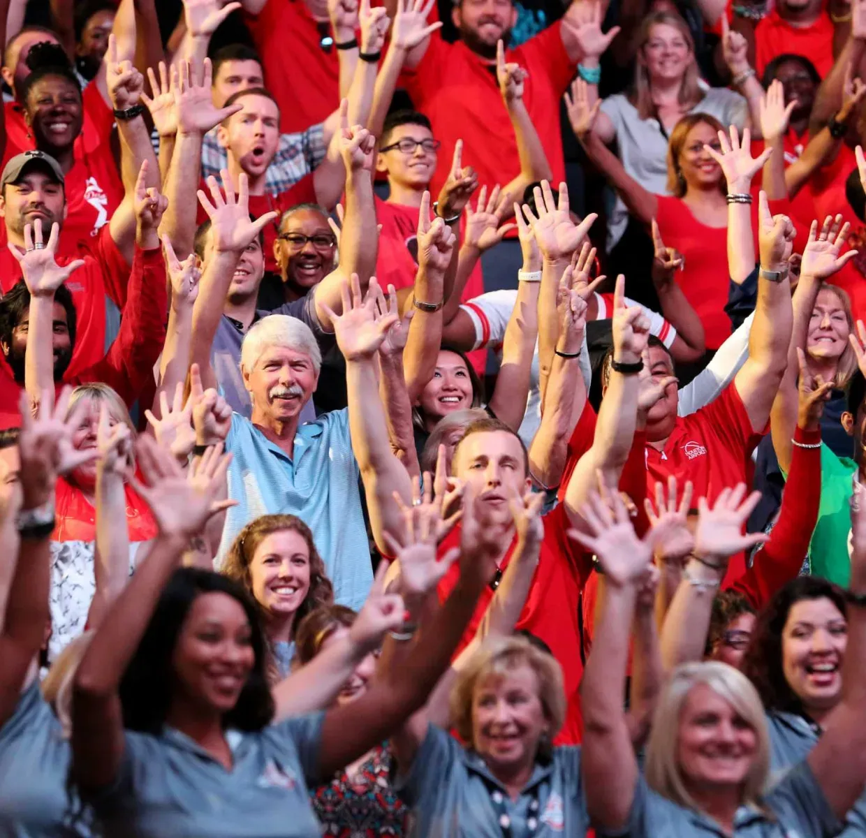 Large group of Super Bowl volunteers in a stadium all dressed in red uniforms with their hands up