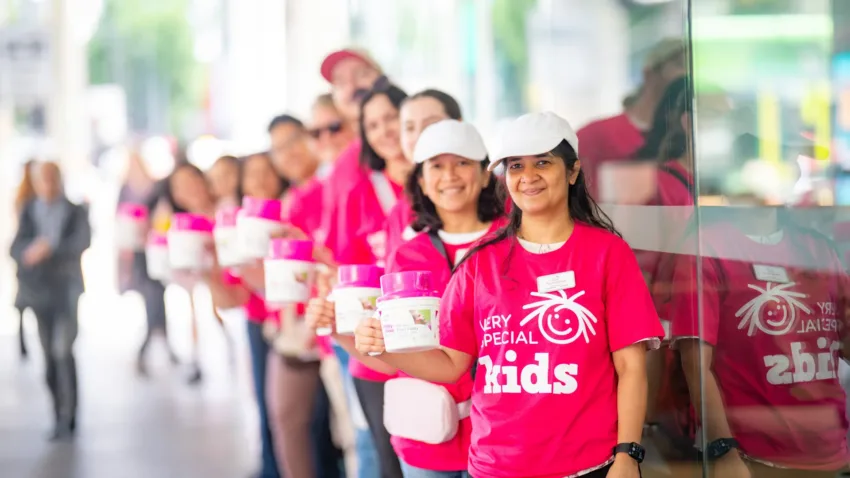 Very Special Kids volunteers in bright pink tshirts holding collection tins for a fundraising event