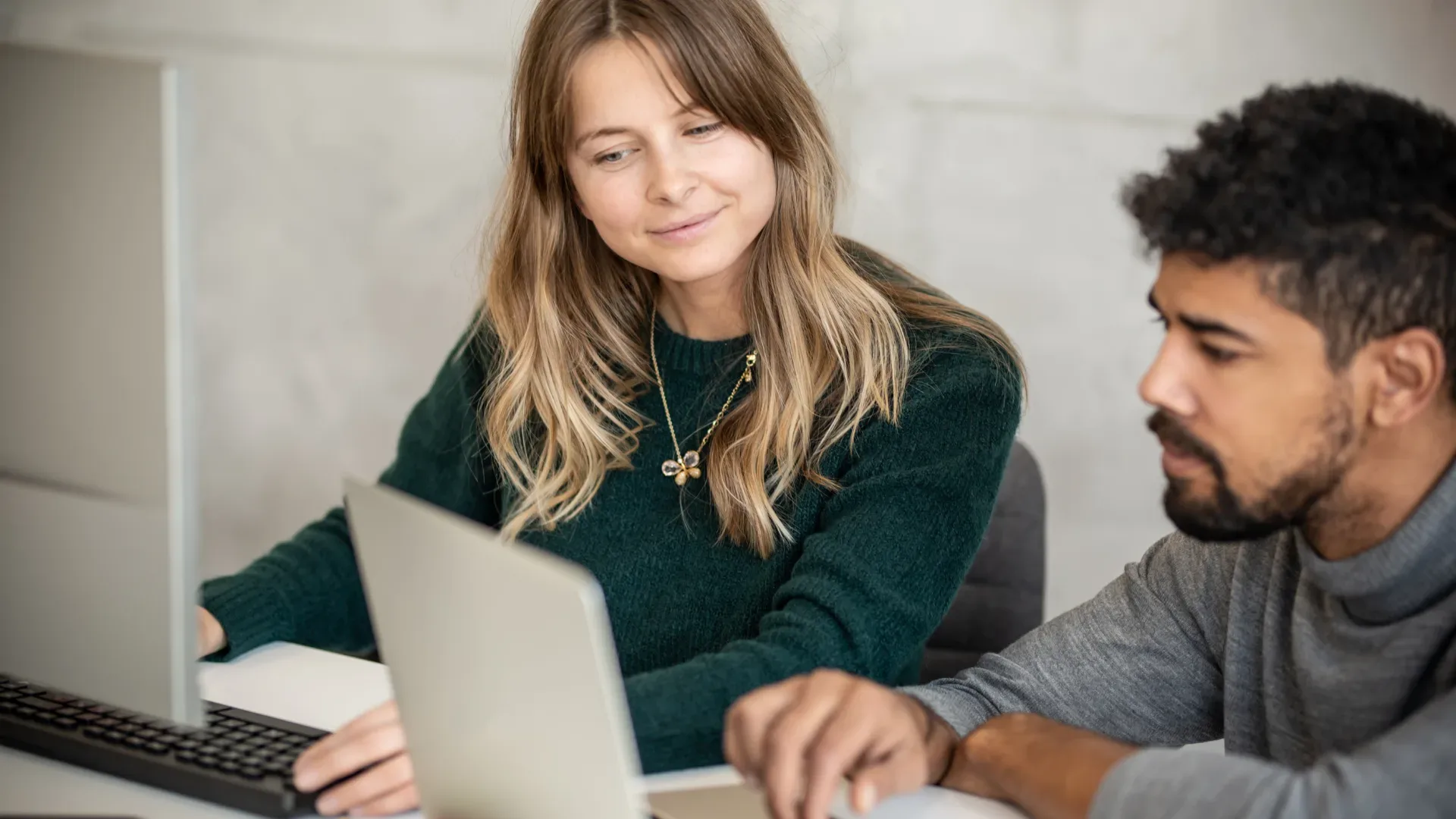 Two colleagues (male and female) working in an office collaborating together looking at the same laptop