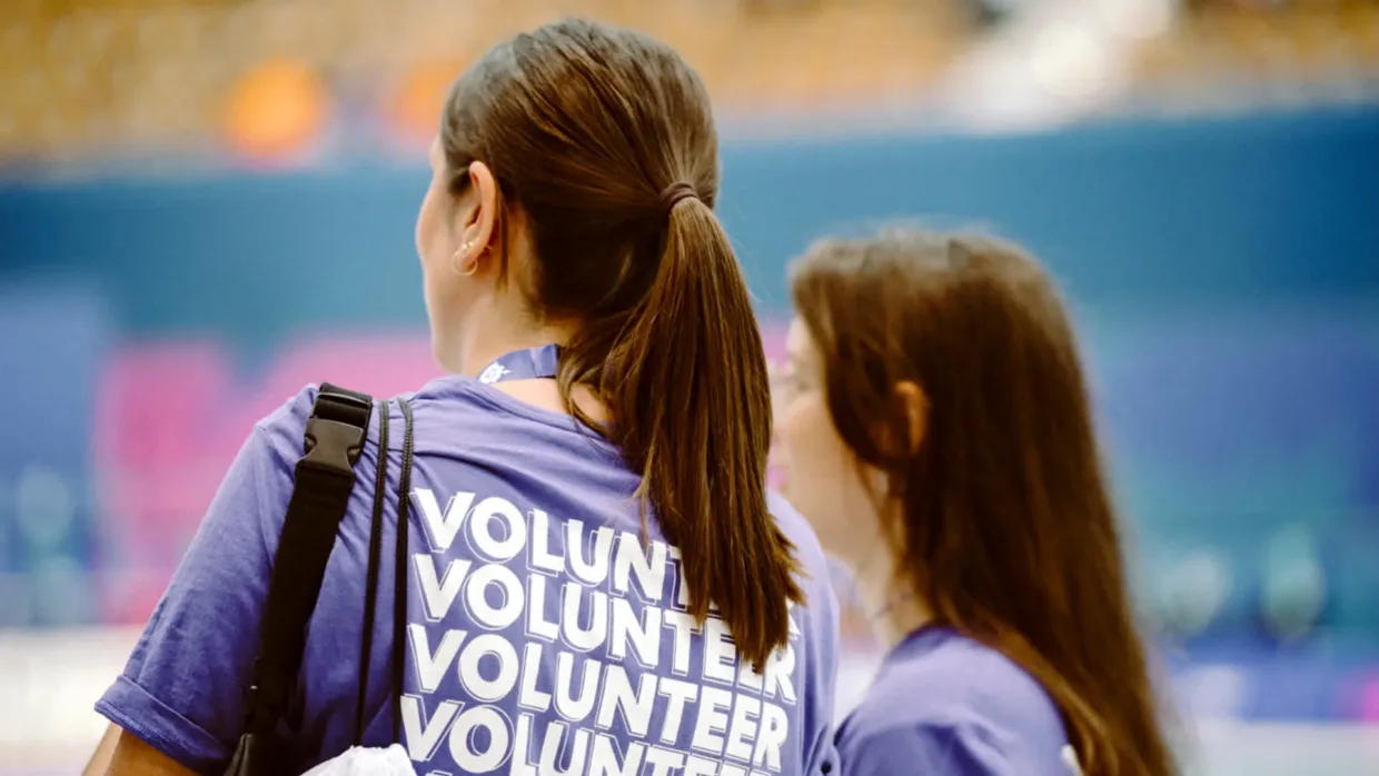 Two volunteers wearing purple tshirts with volunteer written on the back. Volunteers are only shown from their back