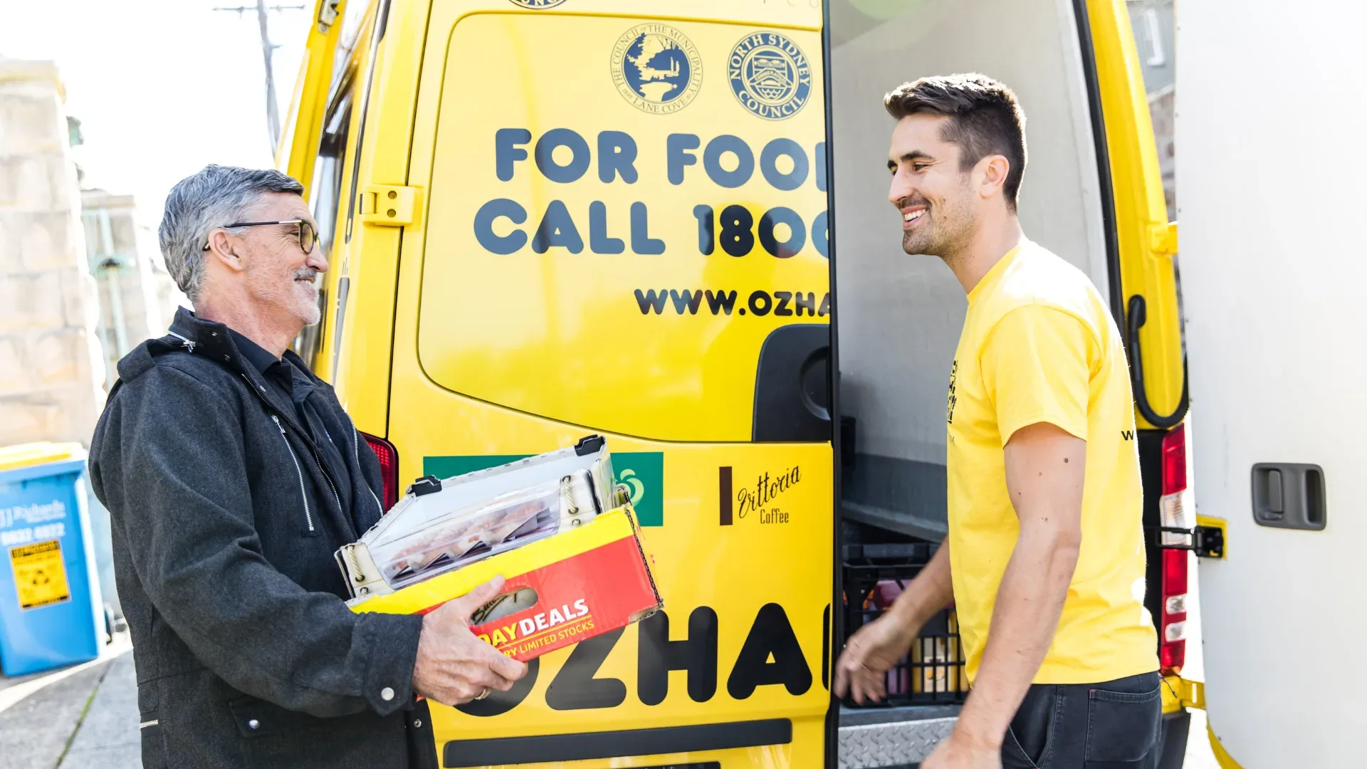 OzHarvest volunteer smiling infront of OzHarvest van collecting a box of food from a man