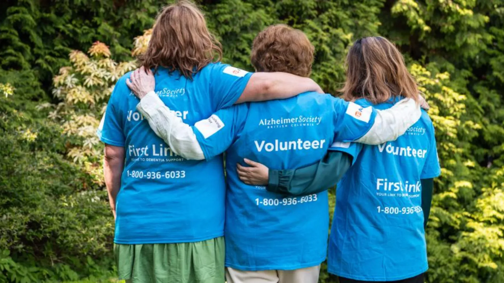 Three volunteers with their backs facing the camera with their arms linked around each other
