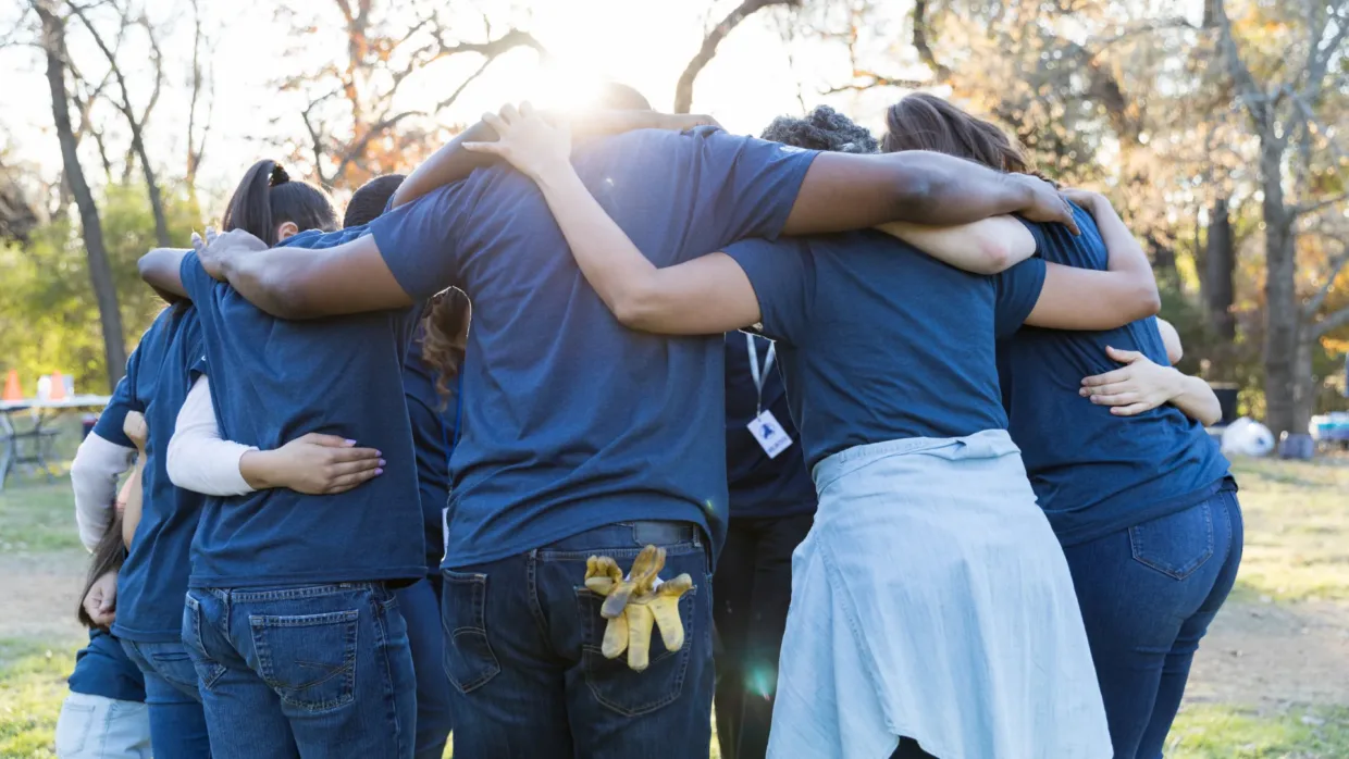 Volunteers in a big team huddle all with their arms around each other in a big circle