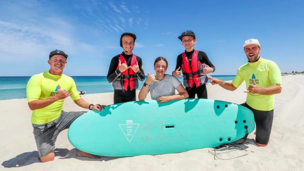 Volunteers on the beach with a surfboard and Ocean Heores particpants
