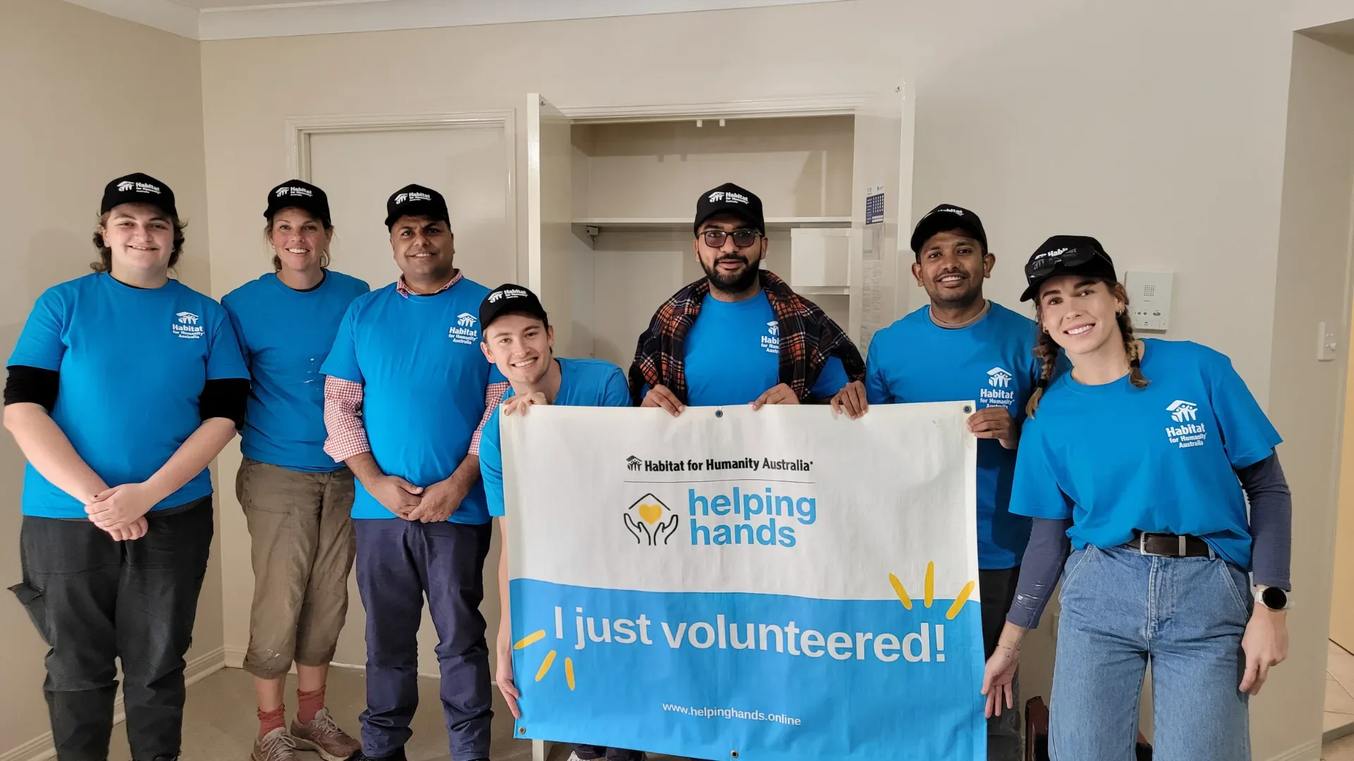 Habitat for Humanity volunteers dressed in blue holding up a sign in a house