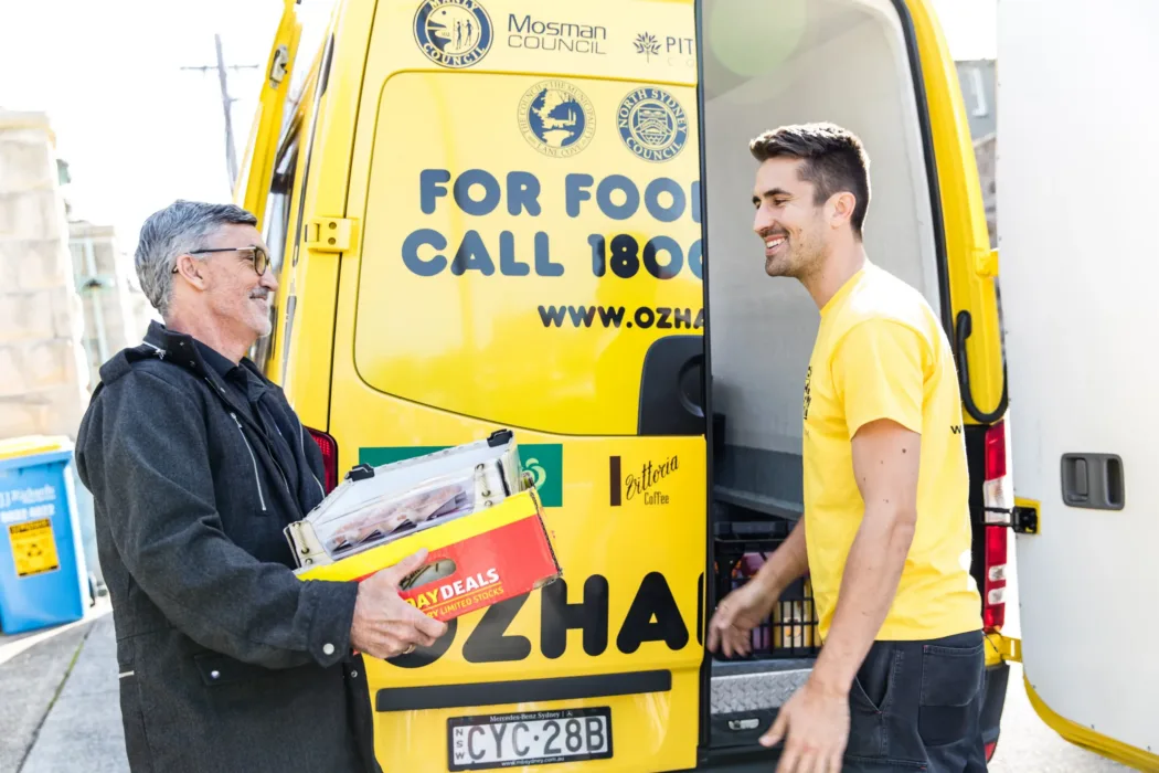 OzHarvest volunteer at back of OzHarvest van collecting food donations from another man holding a crate of food